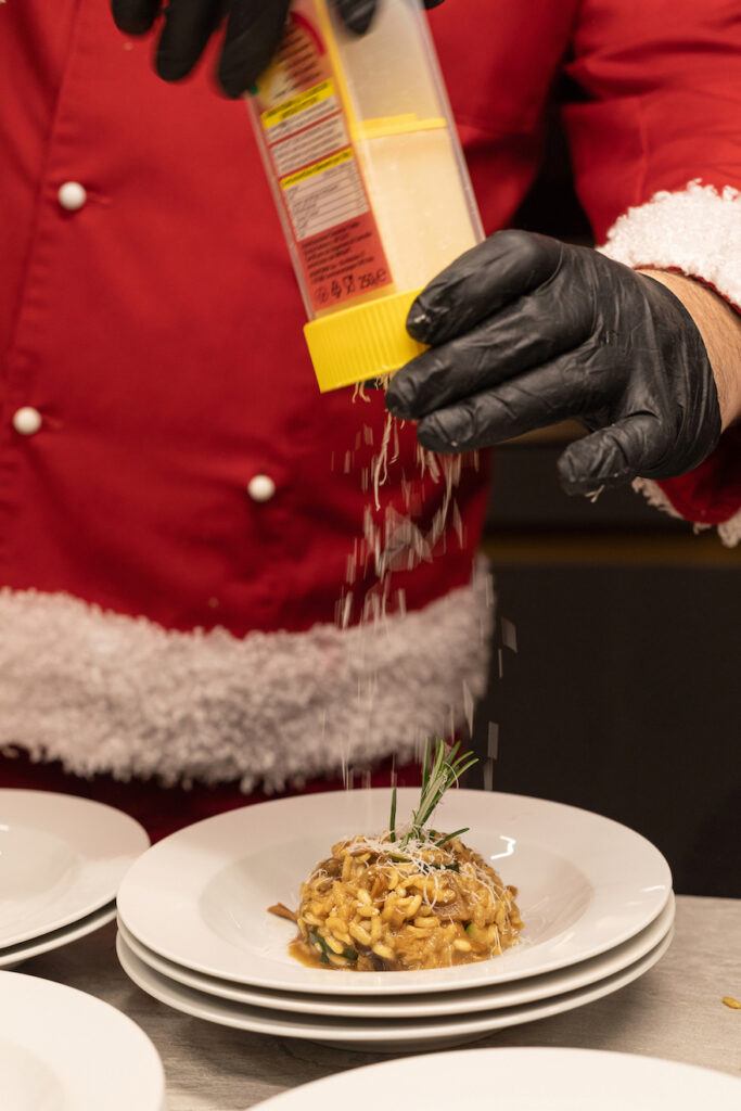 Parmesan wird beim Weihnachtskochen Event im Schauraum Wien ueber das Steinpilzrisotto gerieben und dabei von Fotografin Verena Pelikan fotografiert